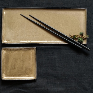 Op de afbeelding: Twee rechthoekige keramische platen, een groter dan de andere, beide in een lichtbruine kleur. Een paar zwarte eetstokjes liggen op de grotere plaat.