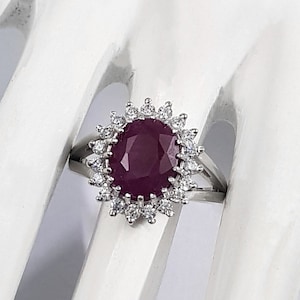 Könnte beinhalten: Ein silberner Ring mit einem großen, ovalen Rubin, der von einem Heiligenschein aus kleineren Diamanten umgeben ist.