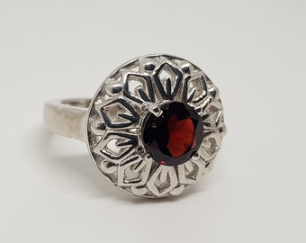 Può includere: Un anello d'argento con una pietra preziosa rossa incastonata in un design delicato e intricato.