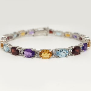 May include: A silver bracelet featuring a row of oval-shaped gemstones in a variety of colours, including amethyst, garnet, topaz, and aquamarine.