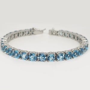 May include: A silver tennis bracelet with a row of round, light blue gemstones.