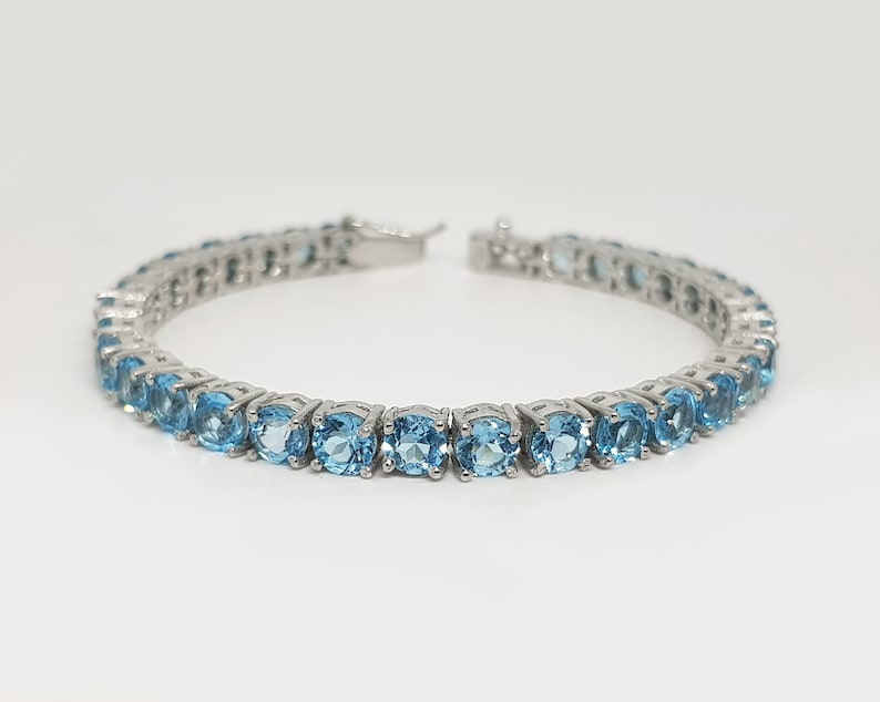 May include: A silver tennis bracelet with a row of round, light blue gemstones.