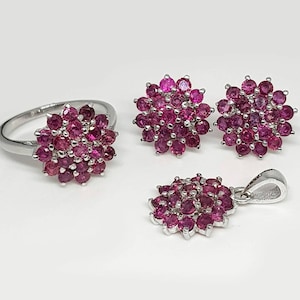 Op de afbeelding: Een zilveren ring, oorbellen en een hangerkettingset met een cluster van roze edelstenen in de vorm van een bloem.