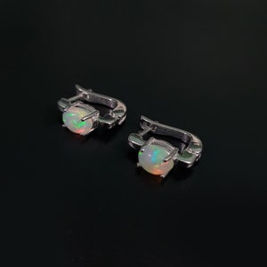 Peut inclure: Une paire de boucles d'oreilles créoles en argent avec une pierre d'opale blanche dans chaque boucle d'oreille.