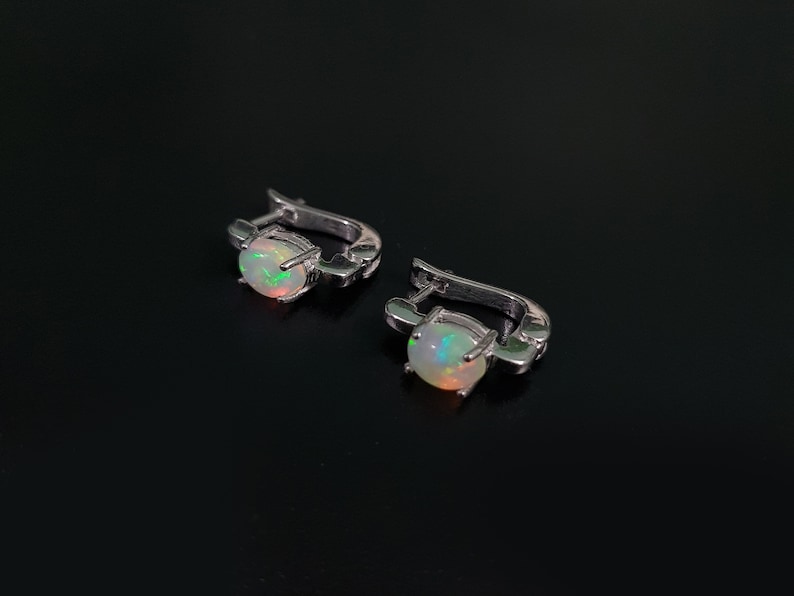 May include: A pair of silver hoop earrings with a white opal gemstone in each earring.