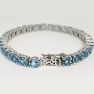 May include: A silver tennis bracelet with a row of light blue round gemstones.