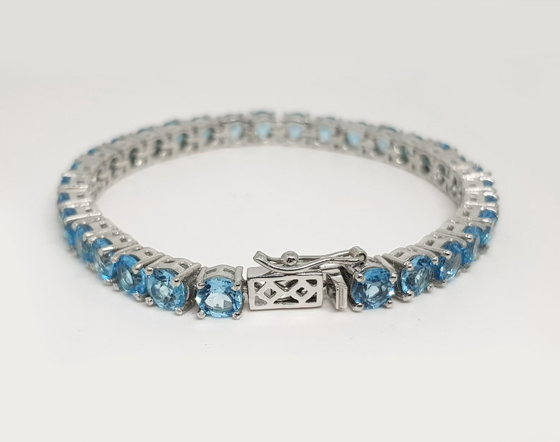 May include: A silver tennis bracelet with a row of light blue round gemstones.