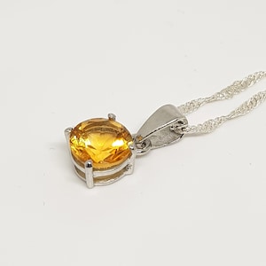 May include: A silver chain necklace with a pendant featuring a round, yellow gemstone.