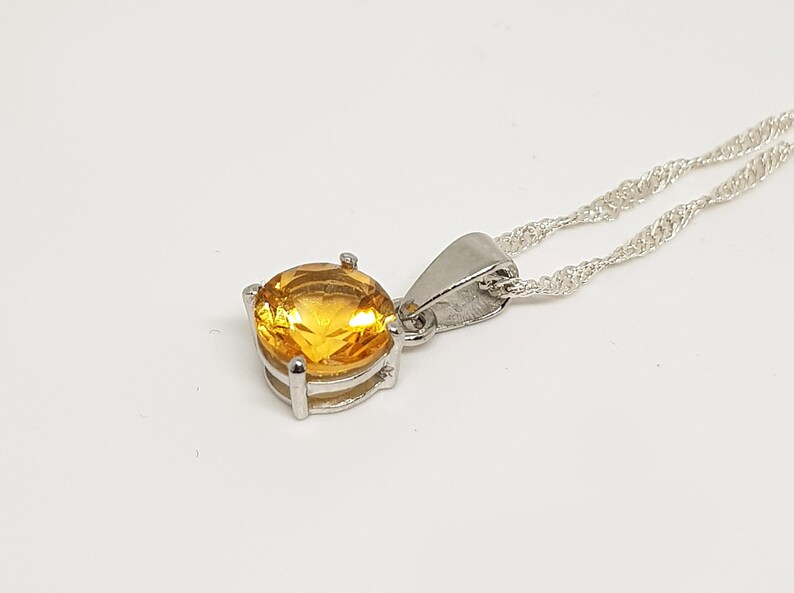 May include: A silver chain necklace with a pendant featuring a round, yellow gemstone.