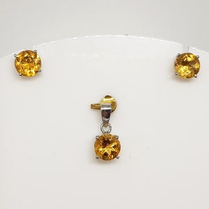 May include: A set of gold and silver earrings and a pendant featuring round, faceted, yellow gemstones.