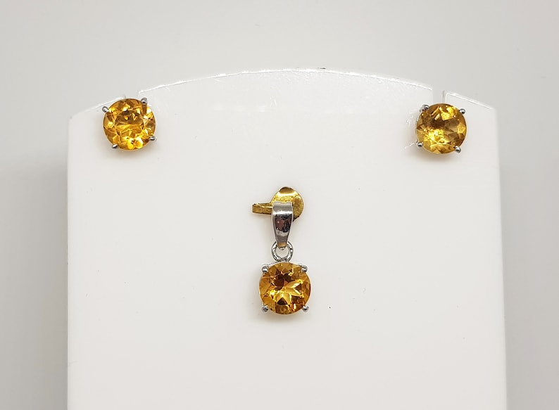 May include: A set of gold and silver earrings and a pendant featuring round, faceted, yellow gemstones.