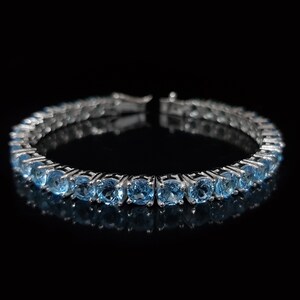 May include: A silver bracelet with a row of round, light blue gemstones. The bracelet is on a black background.