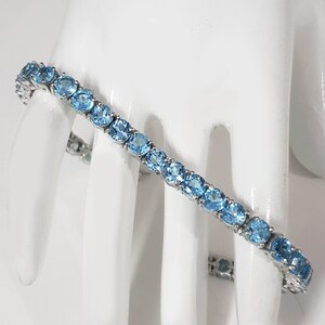 May include: A silver tennis bracelet with a row of oval-shaped blue topaz gemstones.