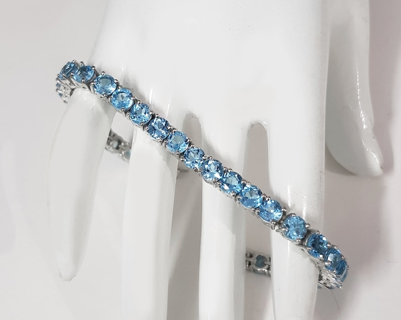 May include: A silver tennis bracelet with a row of oval-shaped blue topaz gemstones.