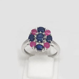 Peut inclure: Une bague en argent avec un groupe de pierres précieuses bleues et roses. La bague est sertie de 10 pierres au total, disposées en cercle.