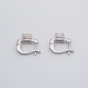 May include: A pair of silver hoop earrings with a white opal gemstone in each earring.