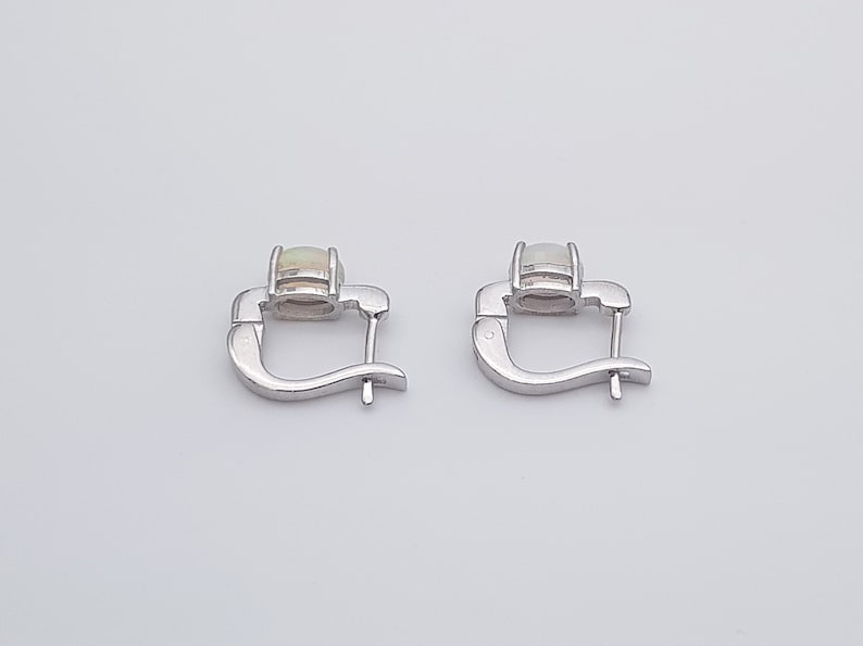 May include: A pair of silver hoop earrings with a white opal gemstone in each earring.