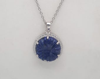 Puede incluir: Un collar de plata con un colgante de piedra azul. El colgante es una flor tallada con un halo de plata de pequeñas piedras transparentes.