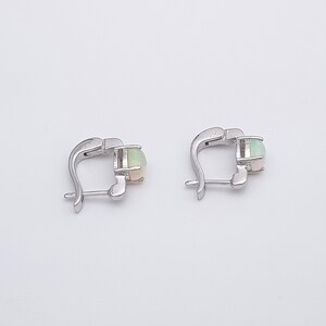 May include: A pair of silver hoop earrings with a round opal gemstone in each earring.
