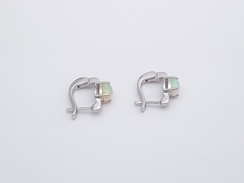 May include: A pair of silver hoop earrings with a round opal gemstone in each earring.
