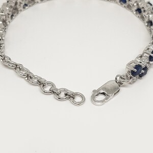 May include: A silver bracelet with two rows of oval, dark blue gemstones. The bracelet has a secure clasp and an adjustable chain. The gemstones are set in a silver metal setting, creating a sparkling effect. Jewelry.