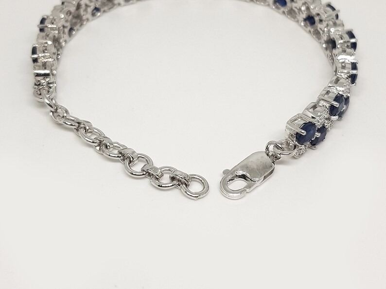 May include: A silver bracelet with two rows of oval, dark blue gemstones. The bracelet has a secure clasp and an adjustable chain. The gemstones are set in a silver metal setting, creating a sparkling effect. Jewelry.