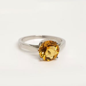 May include: A silver ring with a large, round, yellow topaz gemstone.