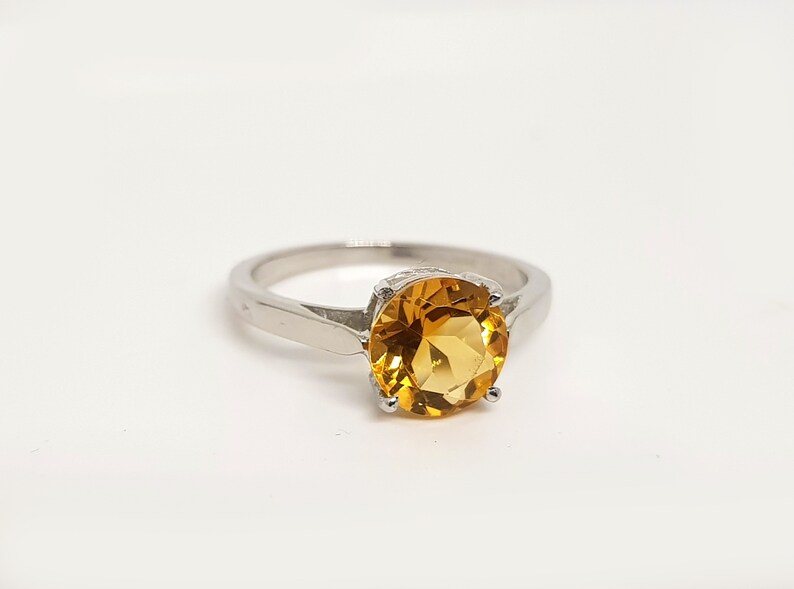 May include: A silver ring with a large, round, yellow topaz gemstone.