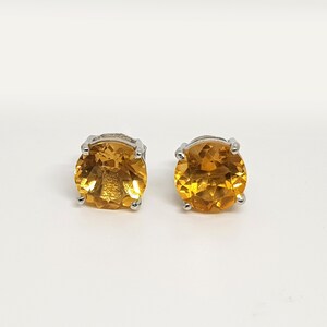May include: A pair of silver stud earrings with round, faceted, orange gemstones.