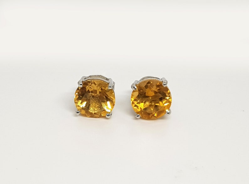 May include: A pair of silver stud earrings with round, faceted, orange gemstones.