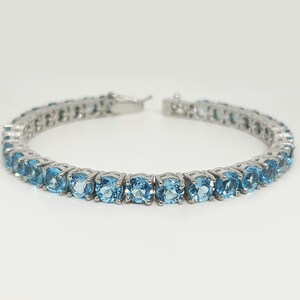 May include: A silver tennis bracelet with a row of light blue round gemstones.