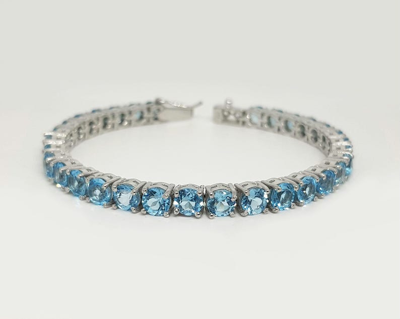 May include: A silver tennis bracelet with a row of light blue round gemstones.
