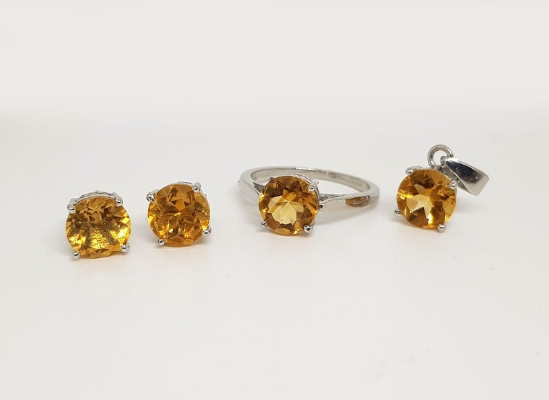 May include: A set of jewelry featuring a ring, earrings, and a pendant, all with round, orange-brown gemstones set in silver.