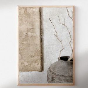 May include: A framed photograph of a rustic still life featuring a gray ceramic vase with a textured surface, filled with dried branches against a white and beige textured wall.