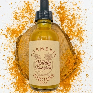 Puede incluir: Una botella de vidrio con un gotero en la parte superior llena de un líquido amarillo. La botella tiene una etiqueta de papel marrón con el texto "Turmeric Wildly Nourished Botanicals Tincture 2 fl oz". La botella está sentada sobre una rodaja de madera rodeada de polvo de cúrcuma amarillo.