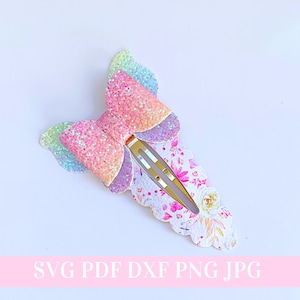 以下が含まれることがあります： 虹色のグリッターの蝶のヘアクリップで、花柄のベースが付いています。クリップは金色で、波打った縁が付いています。