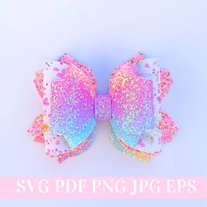 May include: A pink, blue and white layered glitter bow with a floral pattern. The bow is made of fabric and has a shimmery finish.