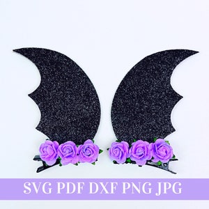 May include: Two black glitter bat wings with purple flower embellishments. The wings are attached to hair clips.
