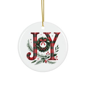 以下が含まれることがあります： 赤と白のチェック柄の文字で「JOY」と書かれた丸い白いクリスマスオーナメント。 「O」は緑のリースに置き換えられています。吊り下げ用の金色の紐が付いています。