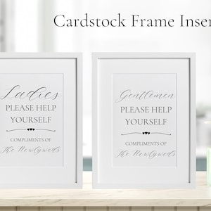 May include: Two white picture frames with black text on white cardstock inserts. The text reads "Ladies Please Help Yourself Compliments of The Newlyweds" and "Gentlemen Please Help Yourself Compliments of The Newlyweds".