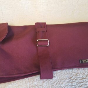 May include: Burgundy dog coat with a buckle fastening and a black label that reads "Fetch Pets Warehouse".