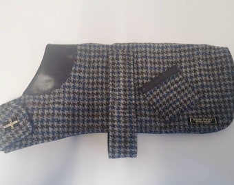 May include: A blue and brown houndstooth dog coat with a leather collar and a pocket on the right side. The coat has a buckle closure and a label that reads "posh paws boutique".