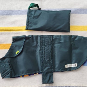 May include: A dark green dog raincoat and matching carrying pouch. The raincoat has a yellow bone-shaped button and a colorful patterned lining. The pouch has a green handle. The raincoat is designed to protect dogs from rain.