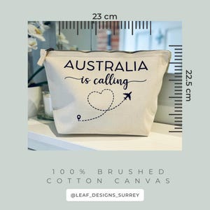 May include: A beige canvas travel pouch with a zipper closure. The text "AUSTRALIA is calling" is printed on the front, along with a heart, airplane, and dotted line design. The pouch measures 23 cm wide and 22.5 cm high.