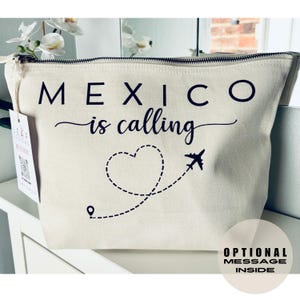 May include: Cream-colored canvas cosmetic bag with a black zipper and the phrase "MEXICO is calling" printed on the front. A dotted heart and airplane graphic are below the text. The bag has a rectangular shape.