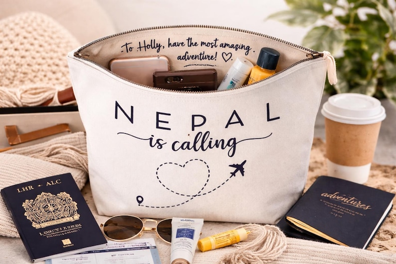 May include: A white canvas travel bag with the text "Nepal is calling" and a heart-shaped dotted line with an airplane. The bag is filled with travel essentials, including a passport, sunglasses, and toiletries.