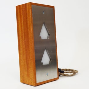 May include: A wooden box with a brushed metal front panel. The panel has two cut-out triangles with white light behind them. The box is connected to a brown cord.