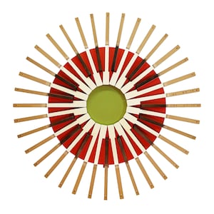 Könnte beinhalten: Runde Wanddekoration mit Sonnenstrahlenmuster. Das Zentrum zeigt einen grünen Kreis, umgeben von roten und weißen Segmenten. Dünne Holzleisten strahlen nach außen und erzeugen einen auffälligen visuellen Effekt. Das Design ist symmetrisch und ansprechend.