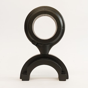 May include: A black, abstract sculpture with a circular top and a curved base. The top features a large, open circle, and the base has a semi-circular design with squared-off ends. The sculpture is made of a solid, dark material and stands on a white surface.