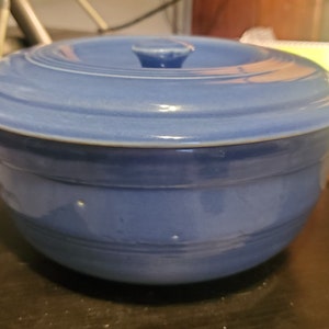 May include: A blue ceramic bowl with a lid. The bowl has a smooth, glazed finish and a slightly rounded shape. The lid has a small knob on top.